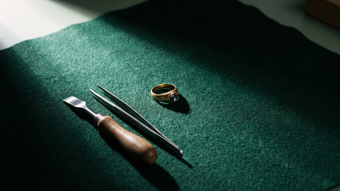 Anello antico con pietra e strumenti da orafo su panno verde