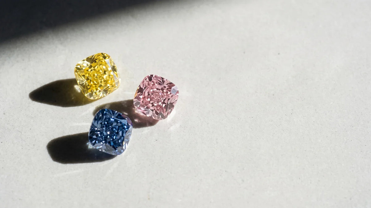 Tre diamanti colorati, giallo rosa e blu, su fondo grigio chiaro